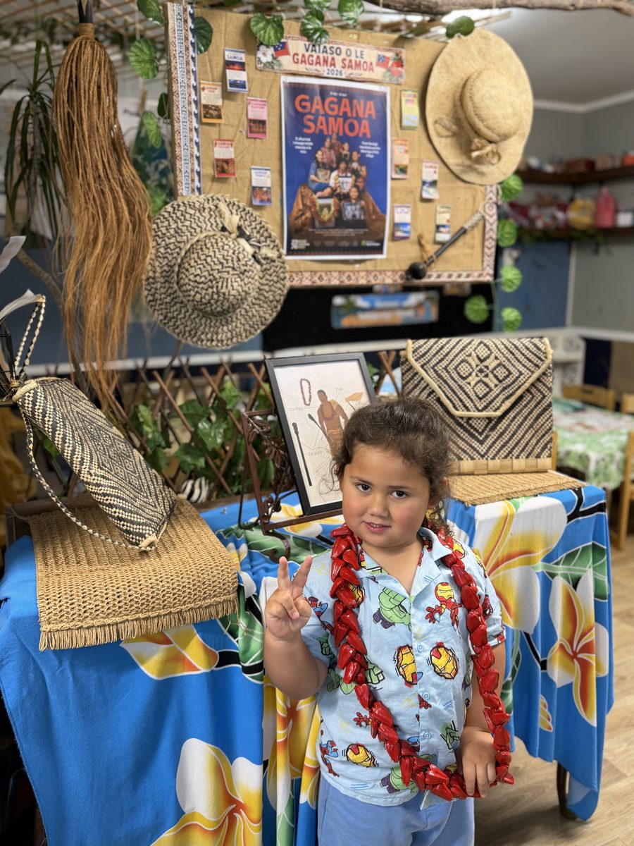 A child beside woven materials and a Gagana Sāmoa display at The Miller Nest