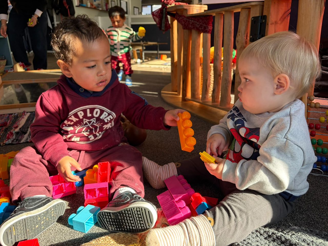 Two infants playing together with colourful construction blocks inside The Miller Nest